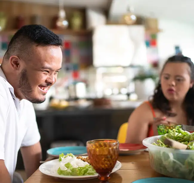 Lächelnder junger Mann und junge Frau genießen eine Mahlzeit in gemütlicher Umgebung.