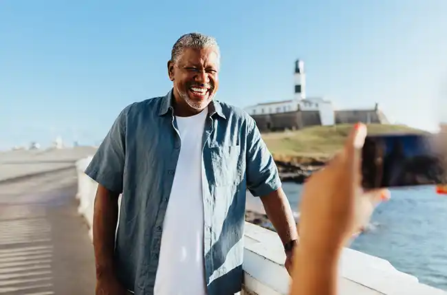 Lachender Mann lässt sich an einer Promenade vor einem Leuchtturm fotografieren.