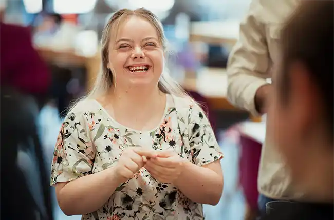 Junge Frau mit Down-Syndrom lacht herzlich in einer Gruppe.