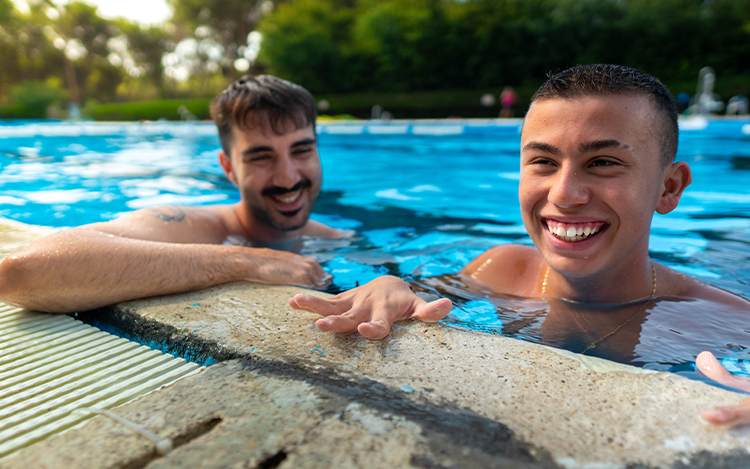 Zwei junge Männer lächeln im Pool und lehnen am Beckenrand