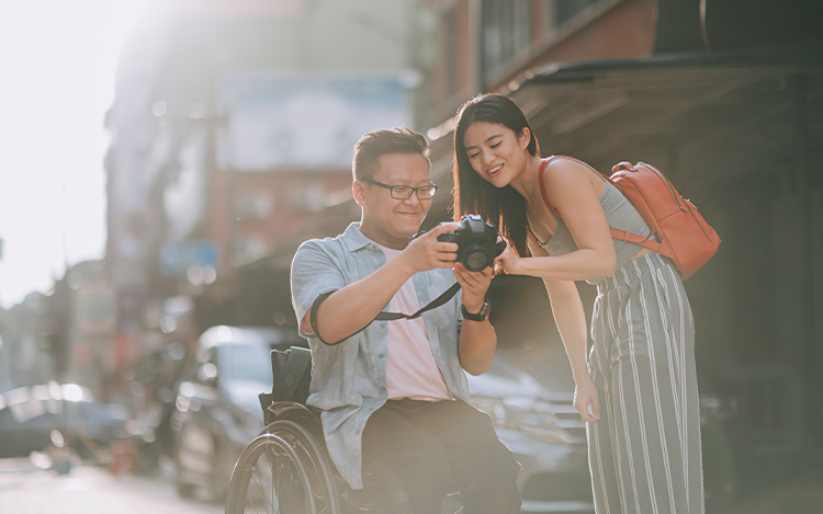 Mann im Rollstuhl zeigt Frau auf Straße ein Foto auf seiner Kamera